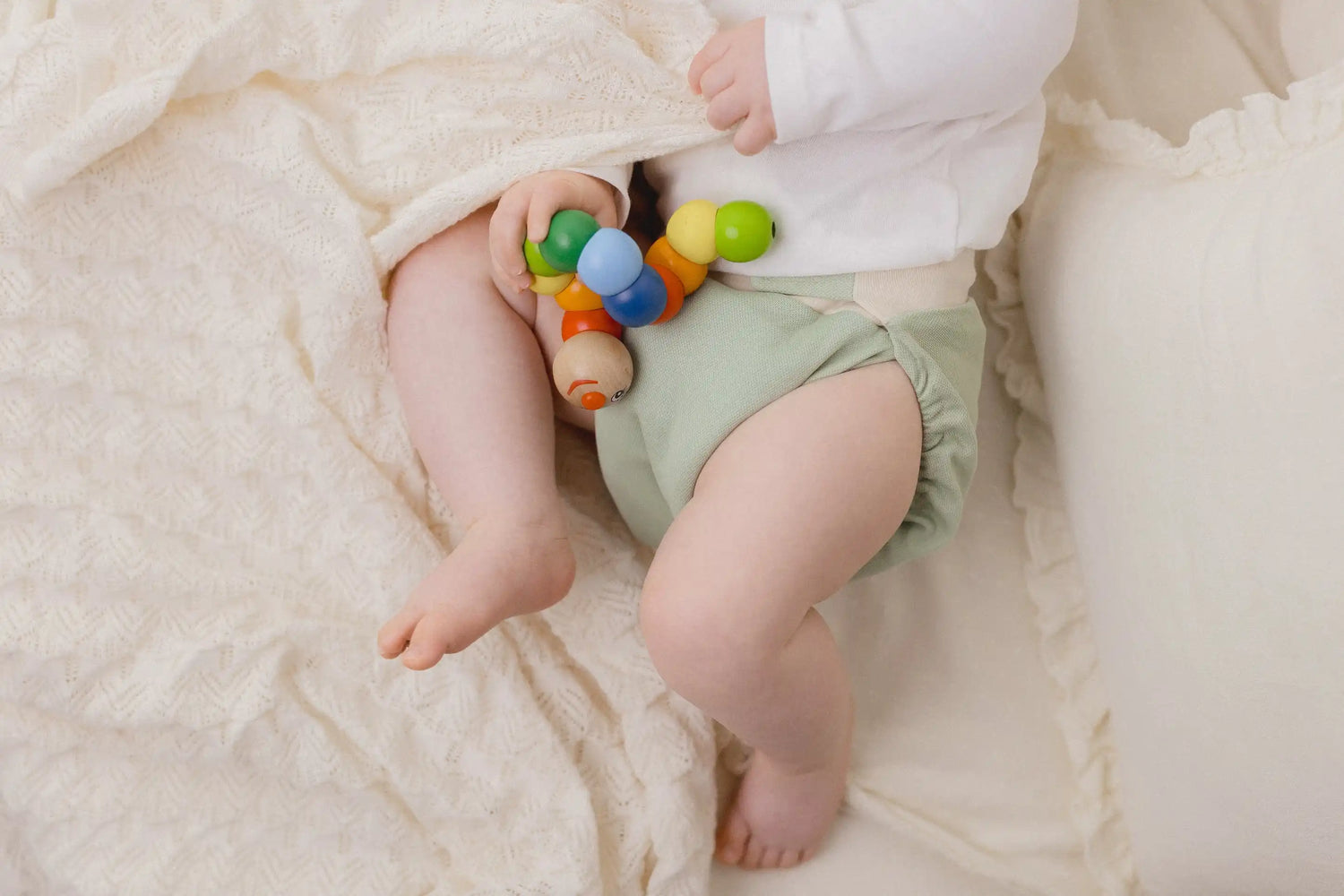 Baby mit kniti an und Spielzeug in der Hand